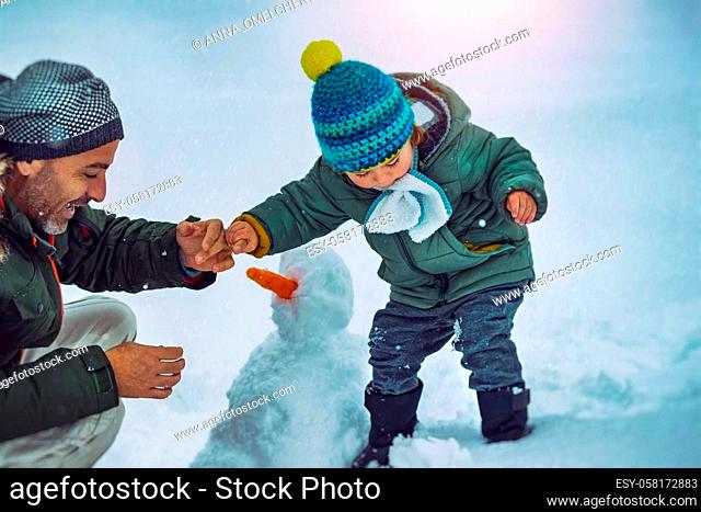 Father and Little Son Building a Snowman in the Snowy Park. Enjoying Time Together Outdoors. Traditional Wintertime Joy. Happy Christmas Holidays
