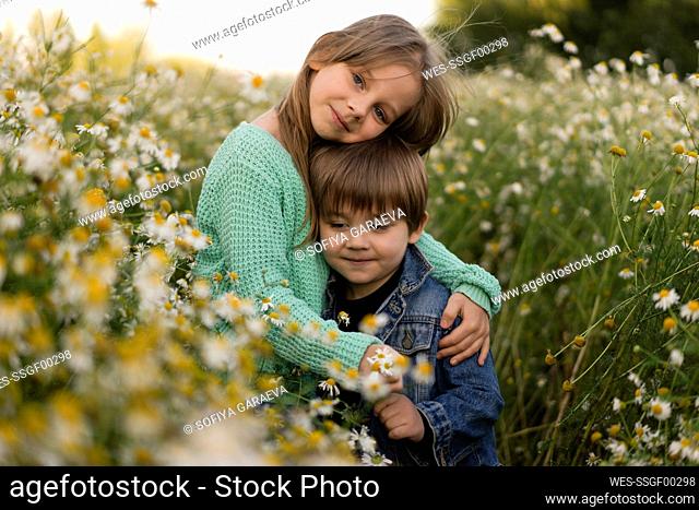 Girl with arm around brother standing amidst flowers in meadow