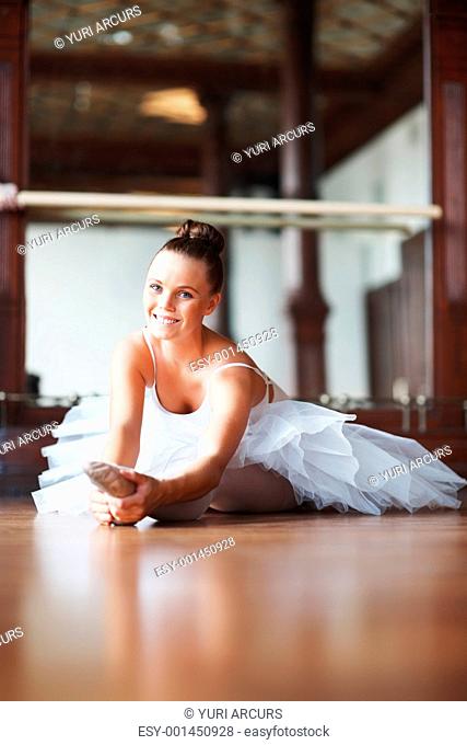 Portrait of a smiling young ballet dancer stretching on dance floor