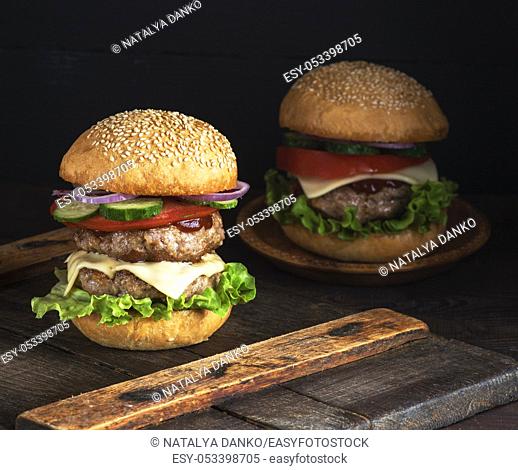 large burger with two fried cutlets, cheese and vegetables in a round wheat flour bun