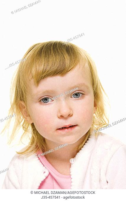 A three year old girl with blonde hair wearing a white sweater appears to be in thought