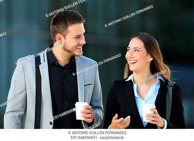 Happy couple of executives walking towards camera and conversing on the street with an office building in the background