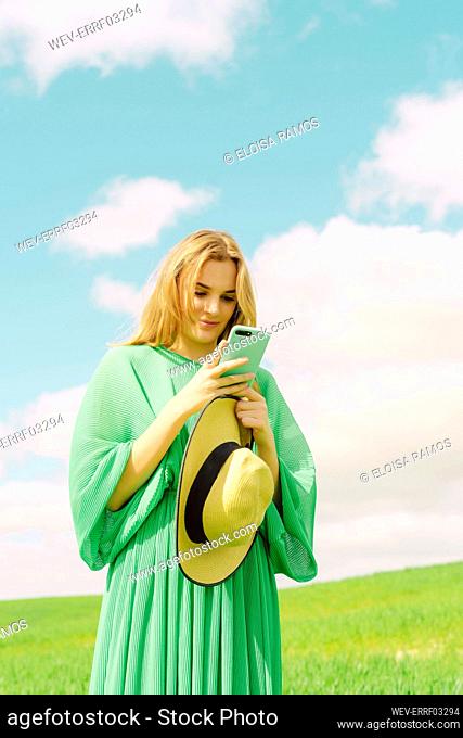 Young woman wearing green dress standing on a field using smartphone