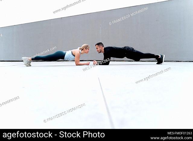 Young couple looking at each other while doing plank against wall