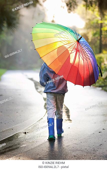 Rear view of boy carrying umbrella on street