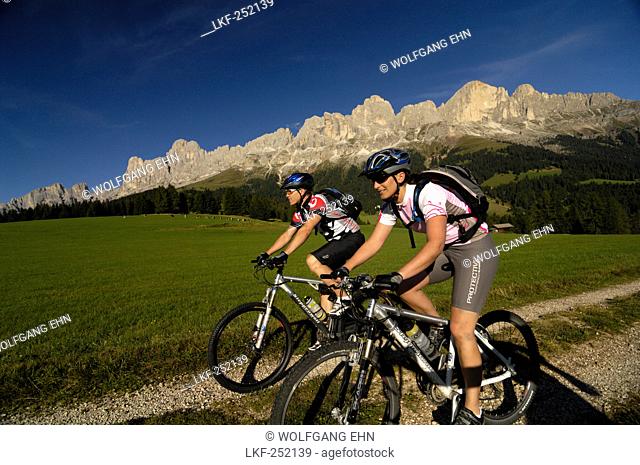 Young couple riding mountain bikes under blue sky, South Tyrol, Italy, Europe