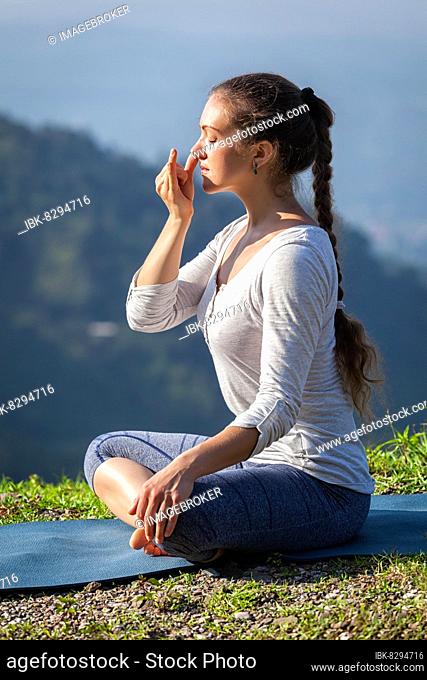 Woman practices pranayama yoga breath control in lotus pose padmasana outdoors in Himalayas in the morning on sunrise. Himachal Pradesh, India, Asia