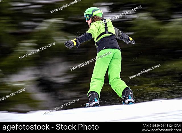 27 March 2021, Hessen, Willingen: A winter sportswoman on a snowboard is skiing downhill at Ettelsberg in Sauerland. The ski season continues until after Easter