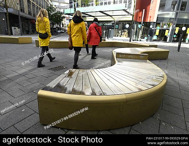 16 October 2023, North Rhine-Westphalia, Wuppertal: Passers-by walk past the shiny gold benches in the pedestrian zone of Elberfeld