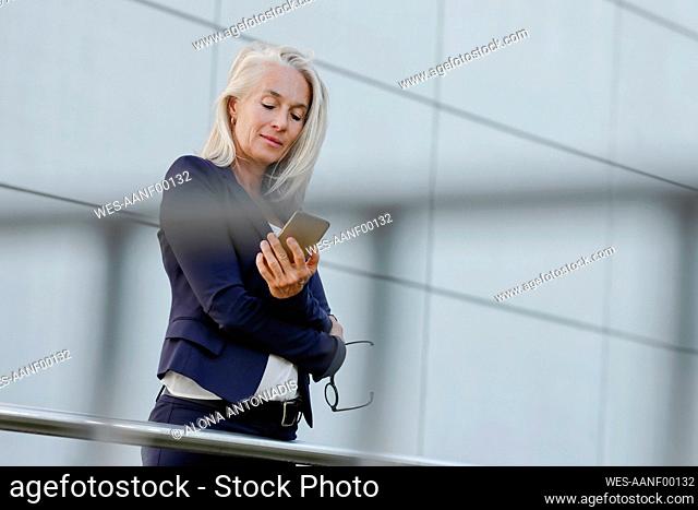 Businesswoman with white hair using smart phone seen through railing