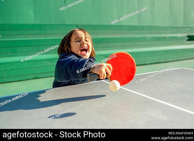 Cheerful boy playing table tennis on sunny day