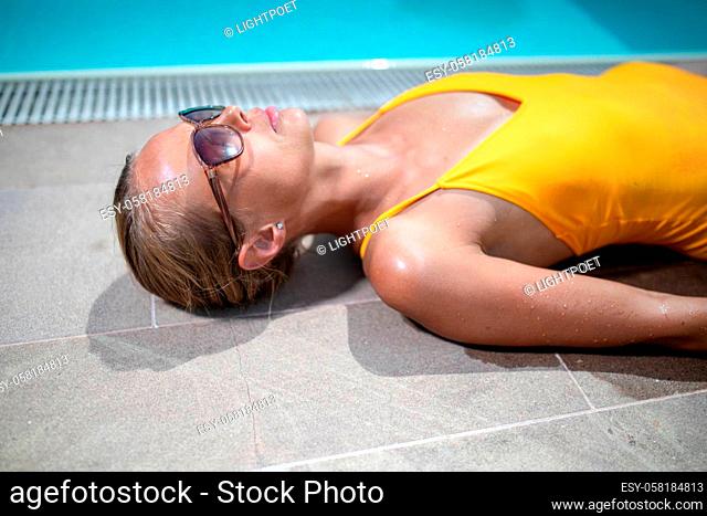 Young Beautiful Suntanned Woman wearing sunglasses relaxing next to a Swimming Pool on a lovely Summer Day
