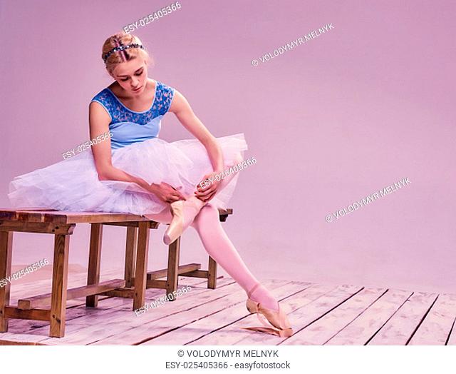 Professional ballerina putting on her ballet shoes on the wooden floor on a pink background