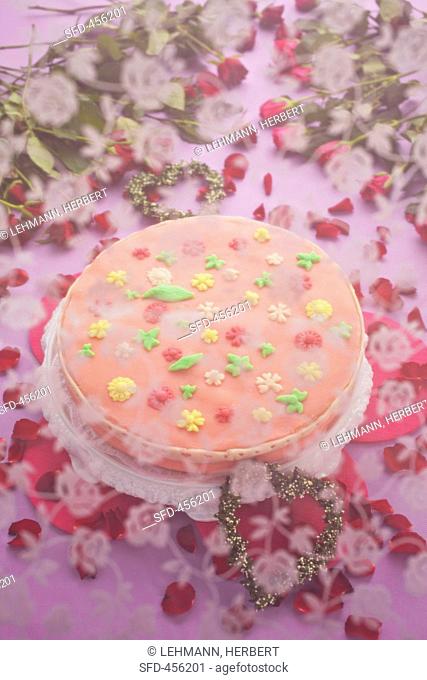 A cake with pink sugar icing and flowers underneath a veil