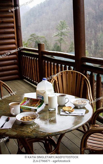 Breakfast table set with milk and cereals on the wooded balcony of a ski resort. The view from the mountains is incredible