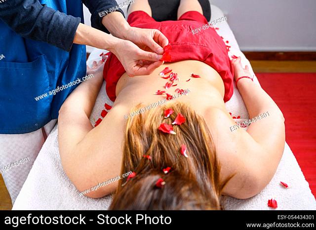 Beautiful woman getting massage and spa treatment with flower petals in spa salon