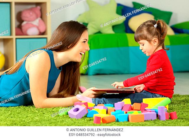 Side view of a mom and toddler playing with a book sitting on a carpet in the bedroom at home