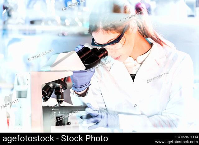 Life scientists researching in laboratory. Focused female young scientist microscoping in scientific working environment