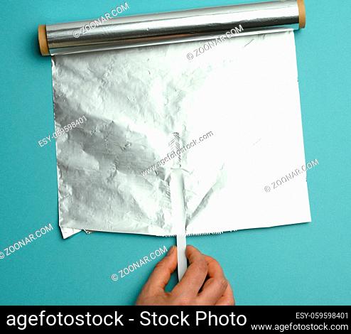 female hand holds an unfolded roll of gray foil on a blue background, close up