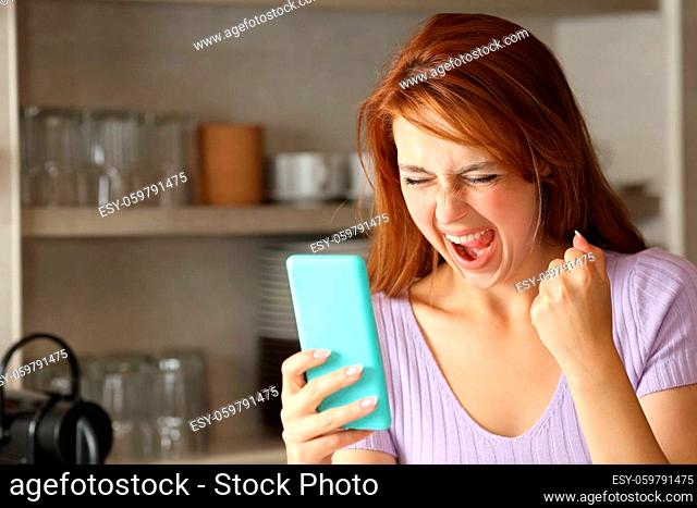 Excited woman checking smart phone content in the kitchen at home