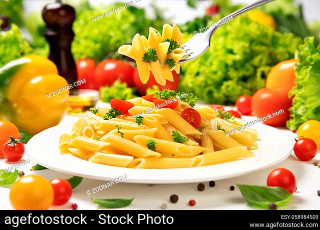 Plate of cooked italian pasta, penne rigate on fork with tomatoes and basil leaves