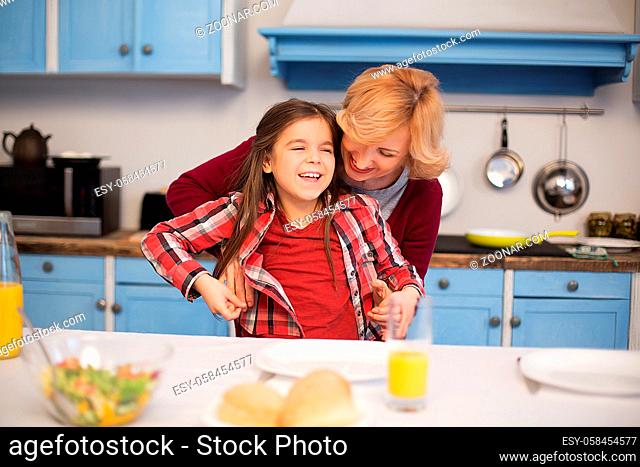 Little pretty girl smiling with her granny in kitchen. Laying table together for dinner