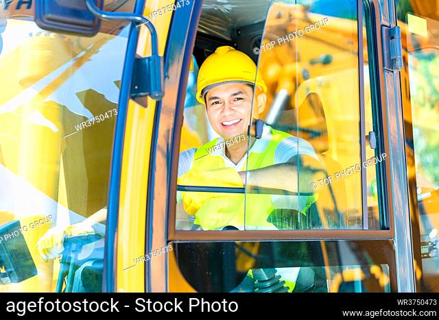 Asian driver sitting in cockpit of construction machinery of building site or mining or rental company