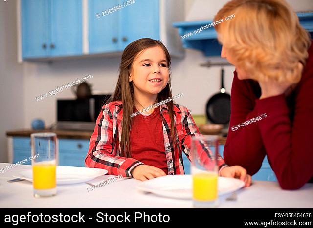 Close up of pretty little girl talking to her granny at atble. Table laying