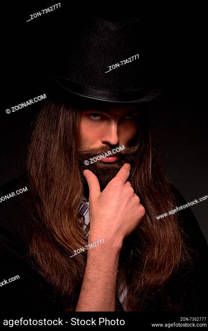 Serious magician gonna to show tricks. Long-haired bearded man keeping moustache isolated on black background