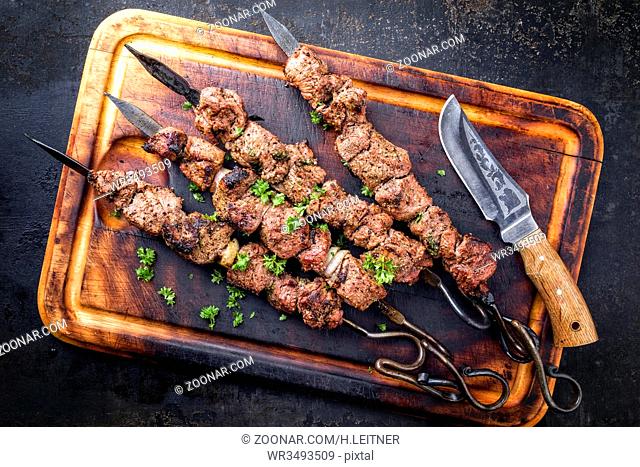 Traditional Russian shashlik on a barbecue skewer as top view on an old burnt cutting board