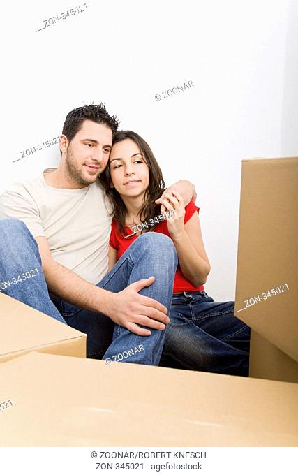 Junges Paar sitzt in einer neuen Wohnung auf dem Boden zwischen vielen Umzugskartons Model l.: Kosta Lales - Model r.: Dimitra Vlahou
