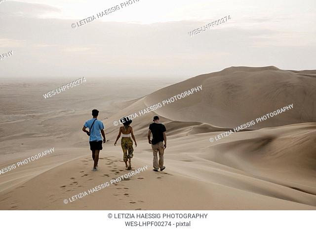 Namibia, Namib, back view of three friends walking side by side on desert dune