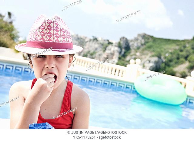 Shot of a Cute Child in Pink Eating a Snack beside the pool