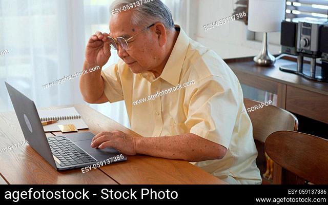 Senior man dressed wear eyeglasses sitting on chair working on laptop in living room at home, Happy old man retired using computer