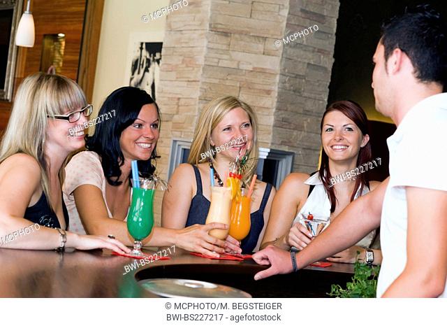 four young women sitting at the bar making goo-goo eyes at young barkeeper serving them cocktails