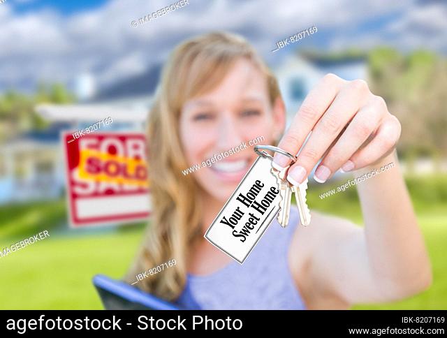 Woman holding new house keys with your home sweet home card in front of sold real estate sign and home