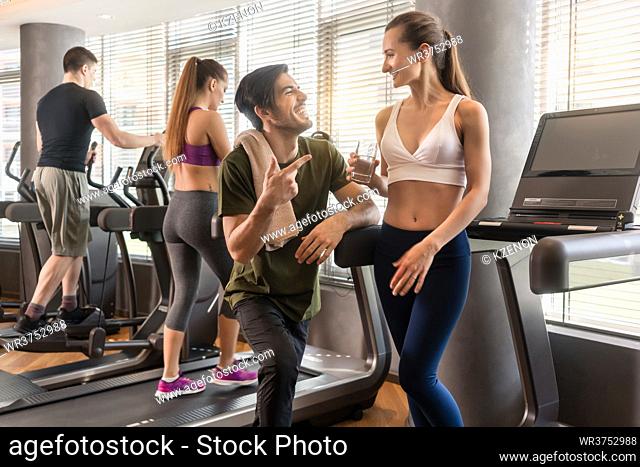 Cheerful young man and woman chatting while having break from running exercise in modern gym