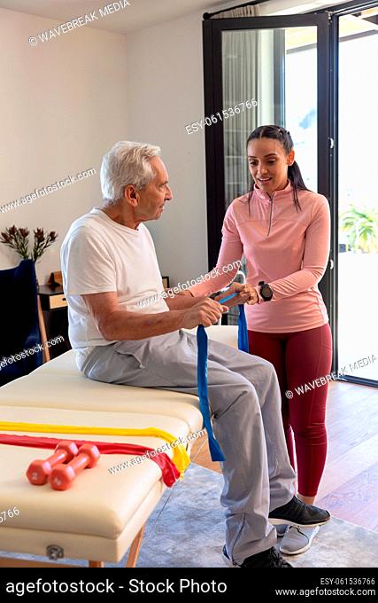 Biracial female physiotherapist helping senior man to exercise with resistance bands