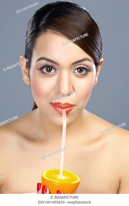 Portrait of a woman drinking juice from an orange