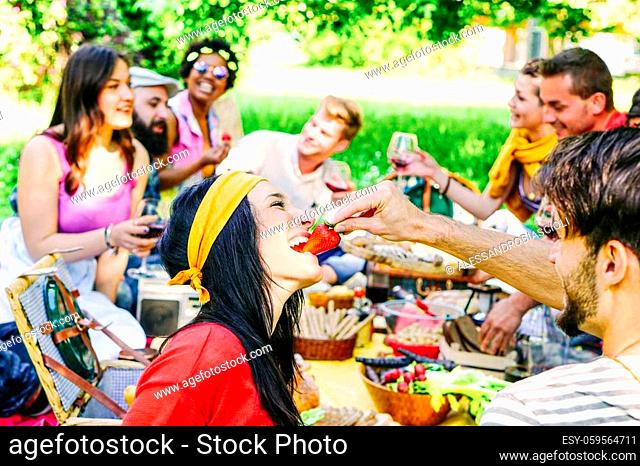 Happy friends making a picnic in the garden outdoor - Young trendy people having fun eating and drinking while sitting on the grass in the nature - Youth