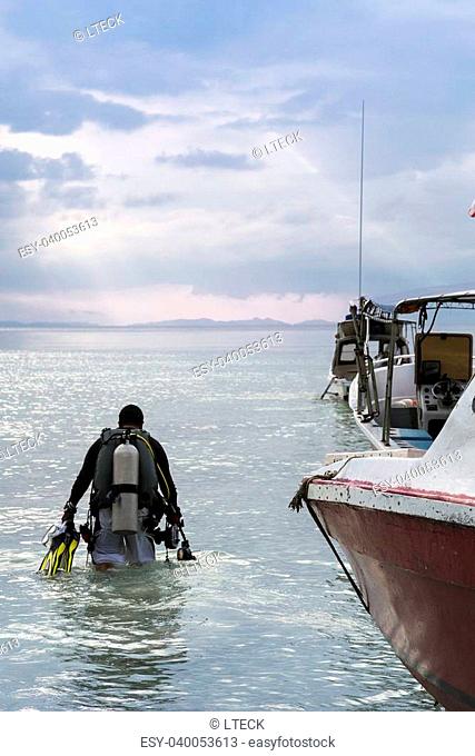 A diver walking towards the ocean with some empty boats beside him