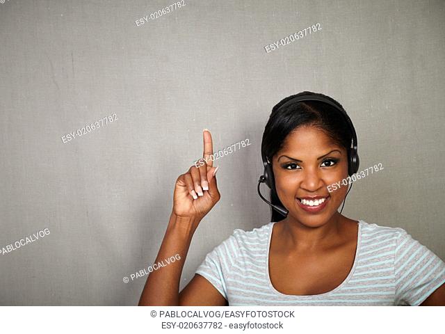 Young receptionist pointing up while smiling against grey texture background
