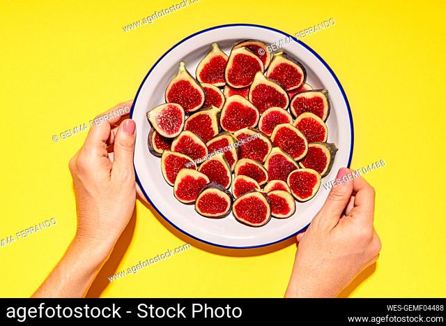 Hands of woman picking up plate with fresh halved figs