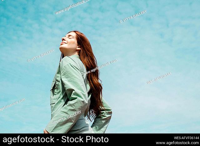 Portrait of redheaded young woman with eyes closed against sky