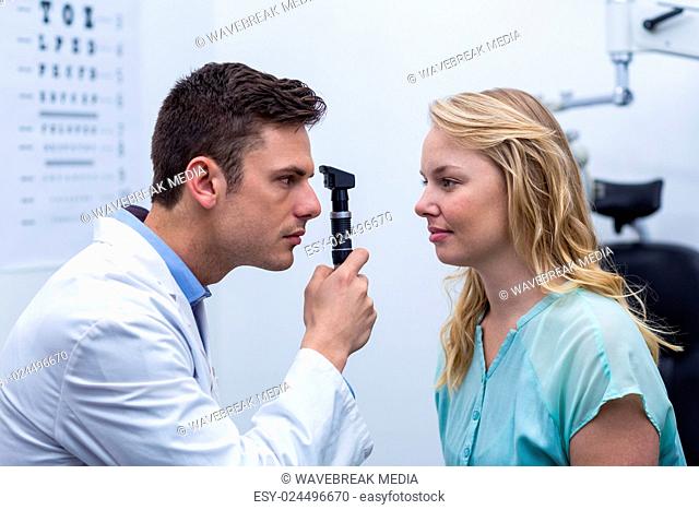 Optometrist examining female patient through ophthalmoscope