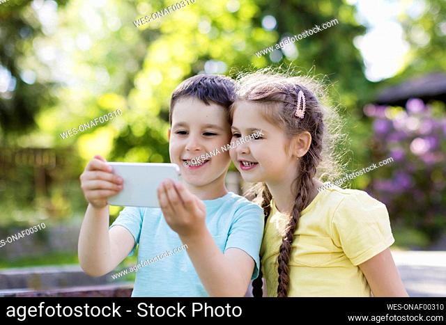 Smiling brother and sister using smart phone in back yard