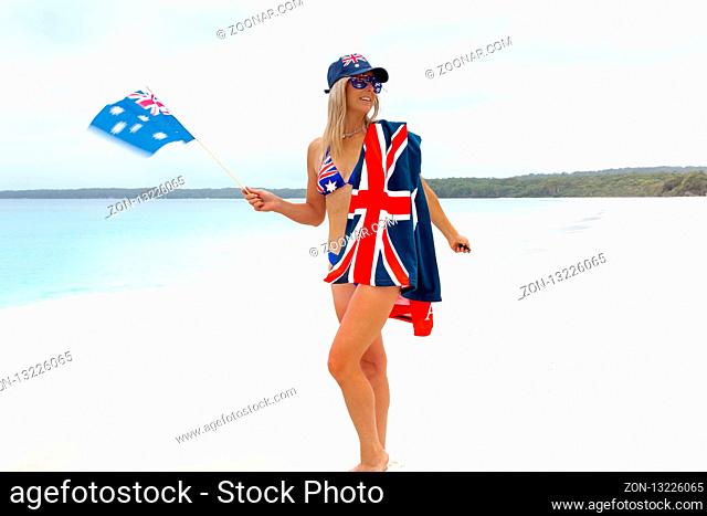 Aussie girl waving an Australian flag on beautifulo pristine beach. She is also has flag printed hat, sunglasses and bikini
