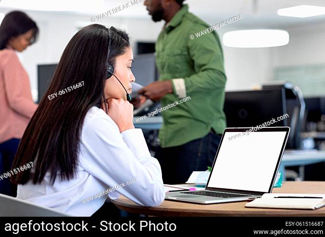 Businesswoman wearing headset using laptop at modern office