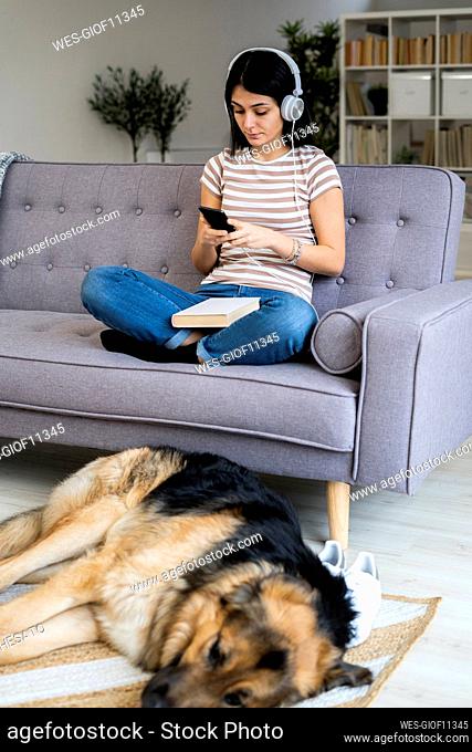Young woman listening music while dog sleeping on carpet in living room