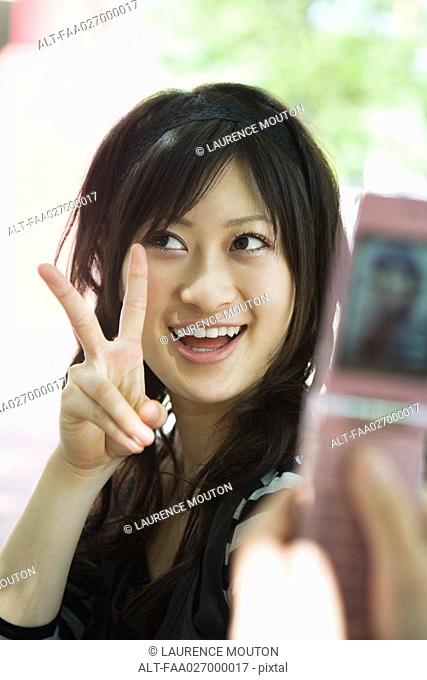 Young woman posing in front of photophone, smiling, holding up peace sign